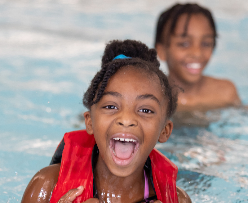 Two children smiling as they swim in the rec pool