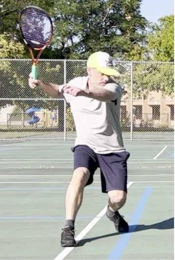 Tennis instructor Christopher N swinging a tennis racket on the court